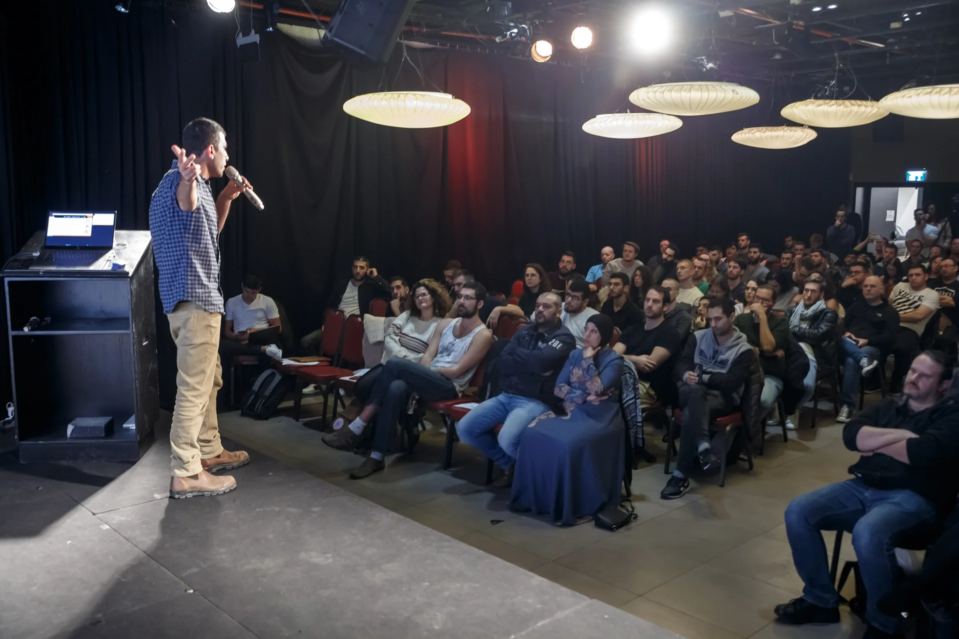 Dani speaking into a microphone in front of a seated auditorium audience